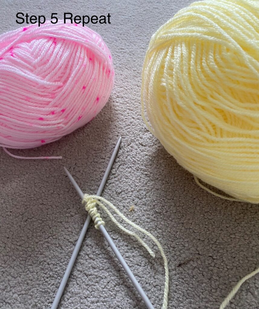Two knitting needles on the carpet, one with several loops of yellow wool on it. There's also a pink ball of wool and a yellow ball of wool on the carpet.
